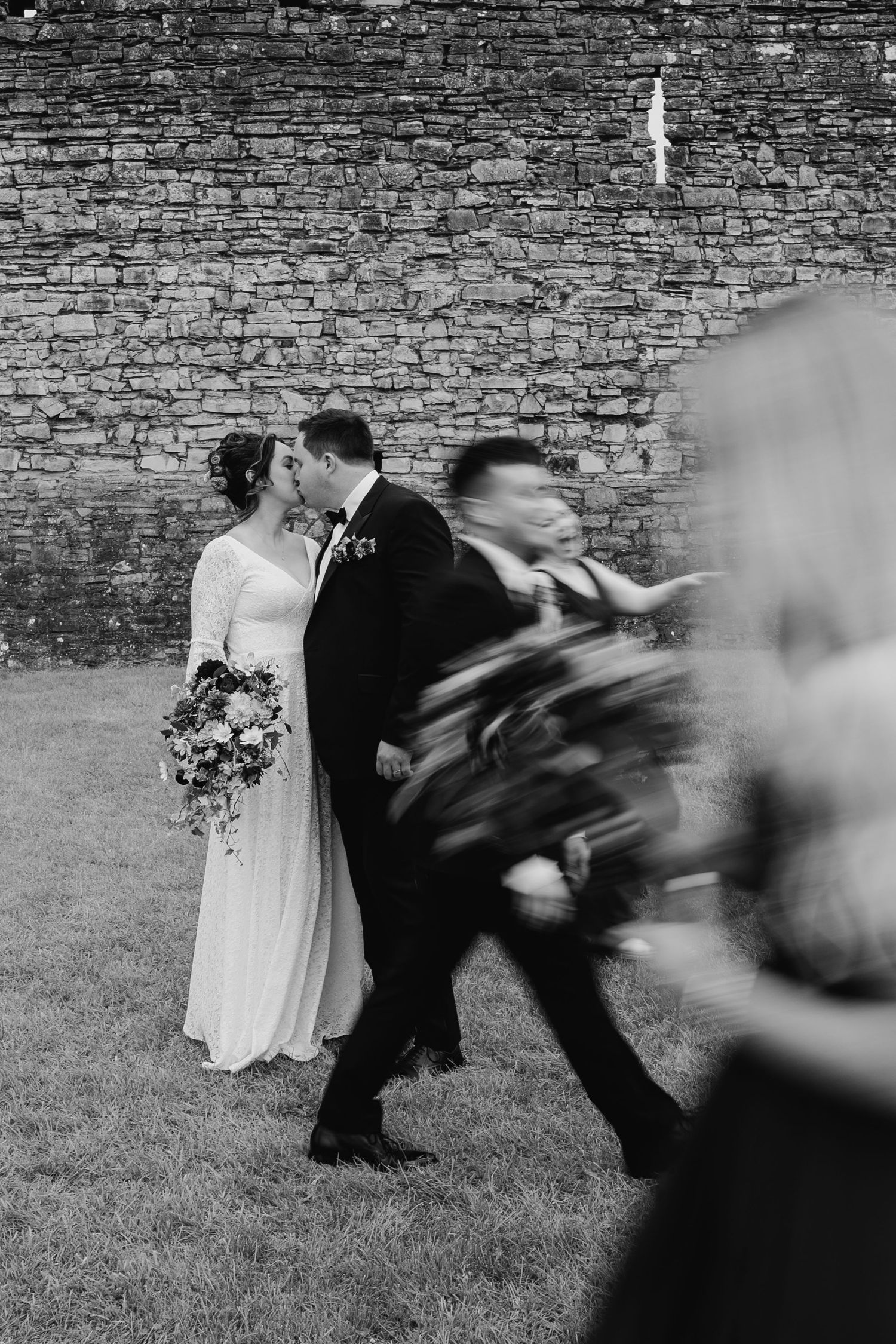 Dramatic black and white sequence of wedding party running past stone wall outdoors. Wedding Photography Trim Castle Ireland