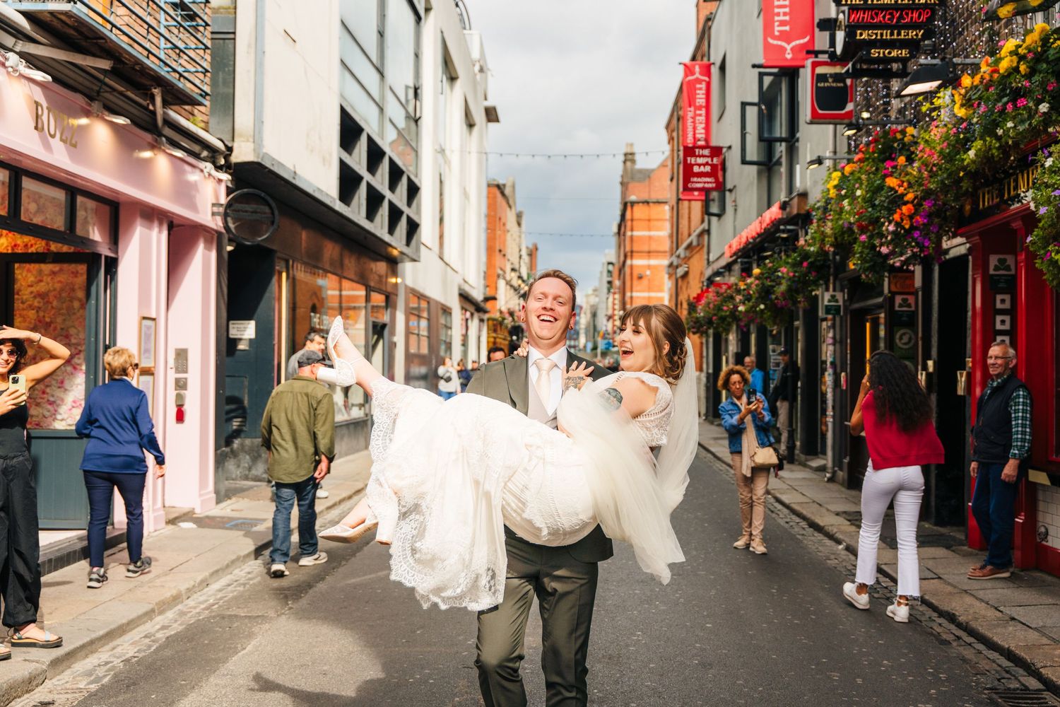 Groom carries bride through charming Dublin street lined with colorful storefronts. PHOTOGRAPHER Dublin Ireland Wedding