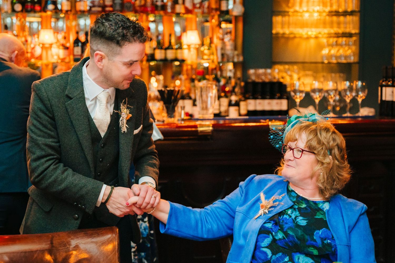 Marco Pierre Dublin Wedding Guests enjoying drinks and conversation at a warmly lit bar with bottles displayed in the background.