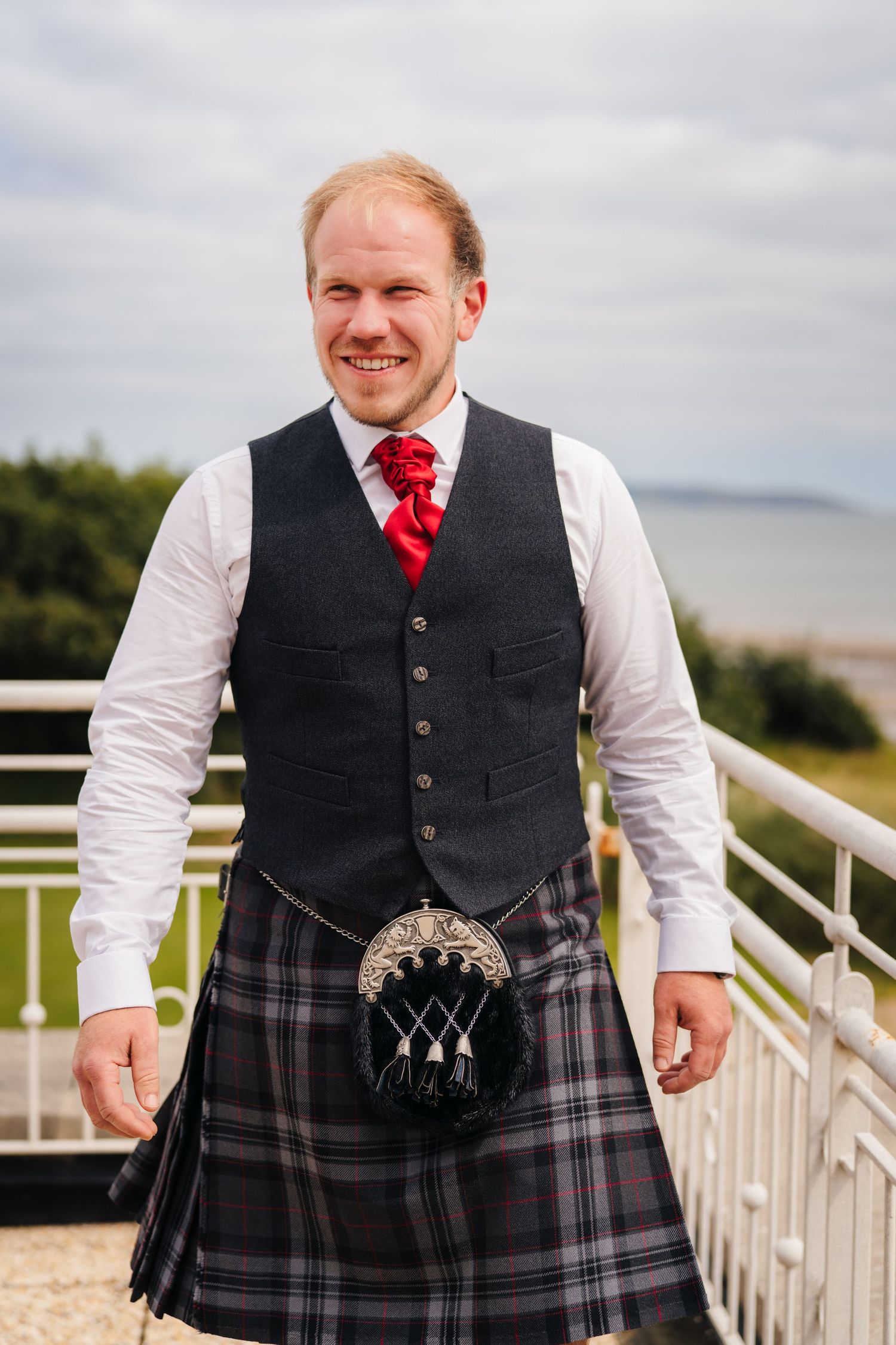 A person wearing traditional Scottish formal wear including a dark waistcoat, white shirt, red tie and tartan kilt with sporran. Portmarnock