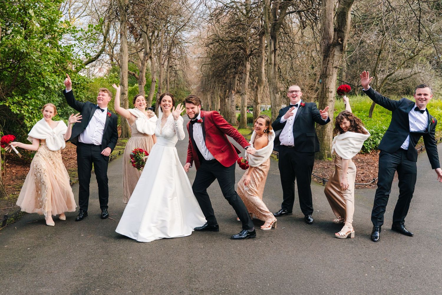 Wedding party poses playfully in a row outdoors with formal attire and natural backdrop. Stephens green club dublin Wedding photographer