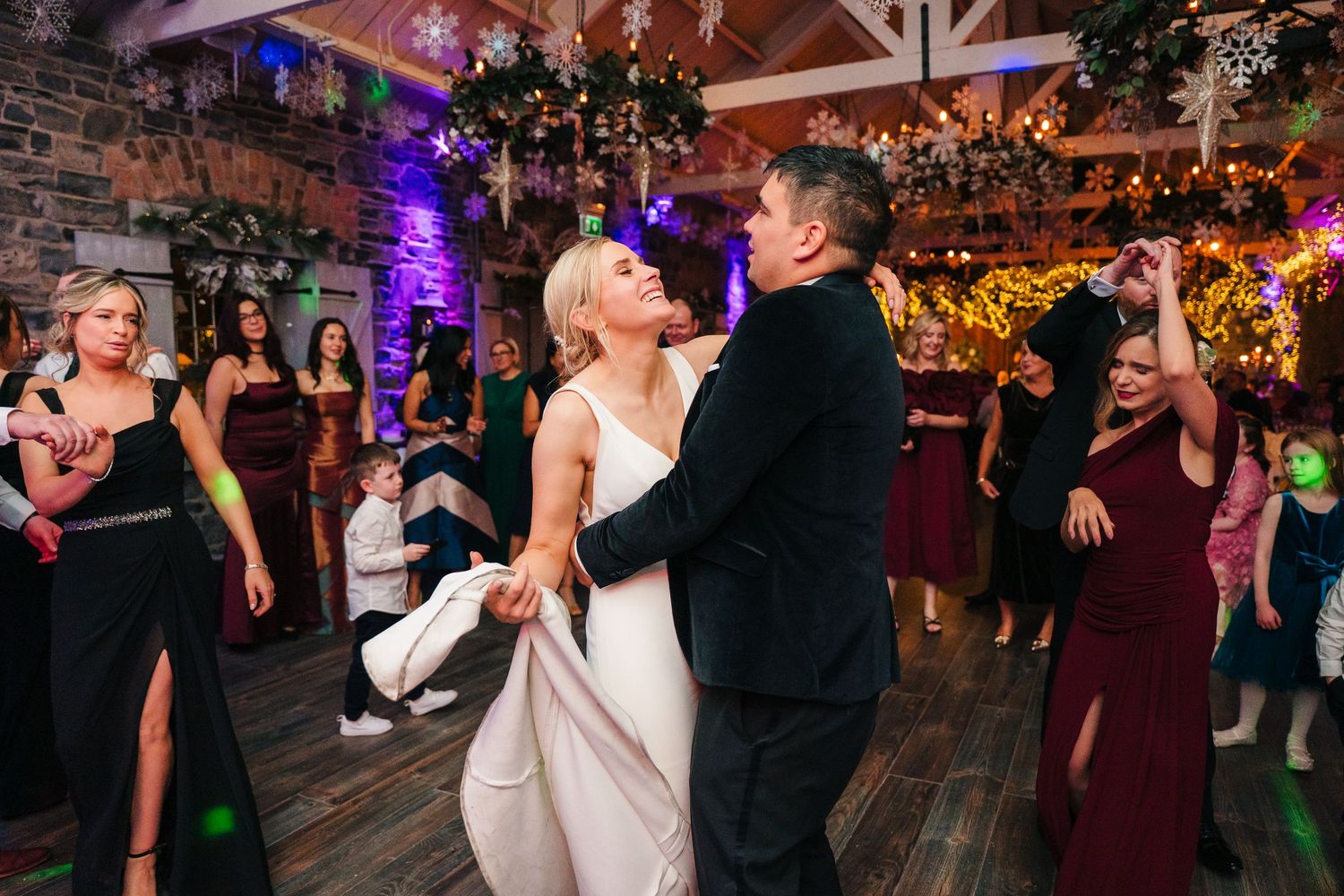 Wedding reception dance floor filled with celebration under purple mood lighting and rustic wooden beams. Ballymagarvey Wedding photographer