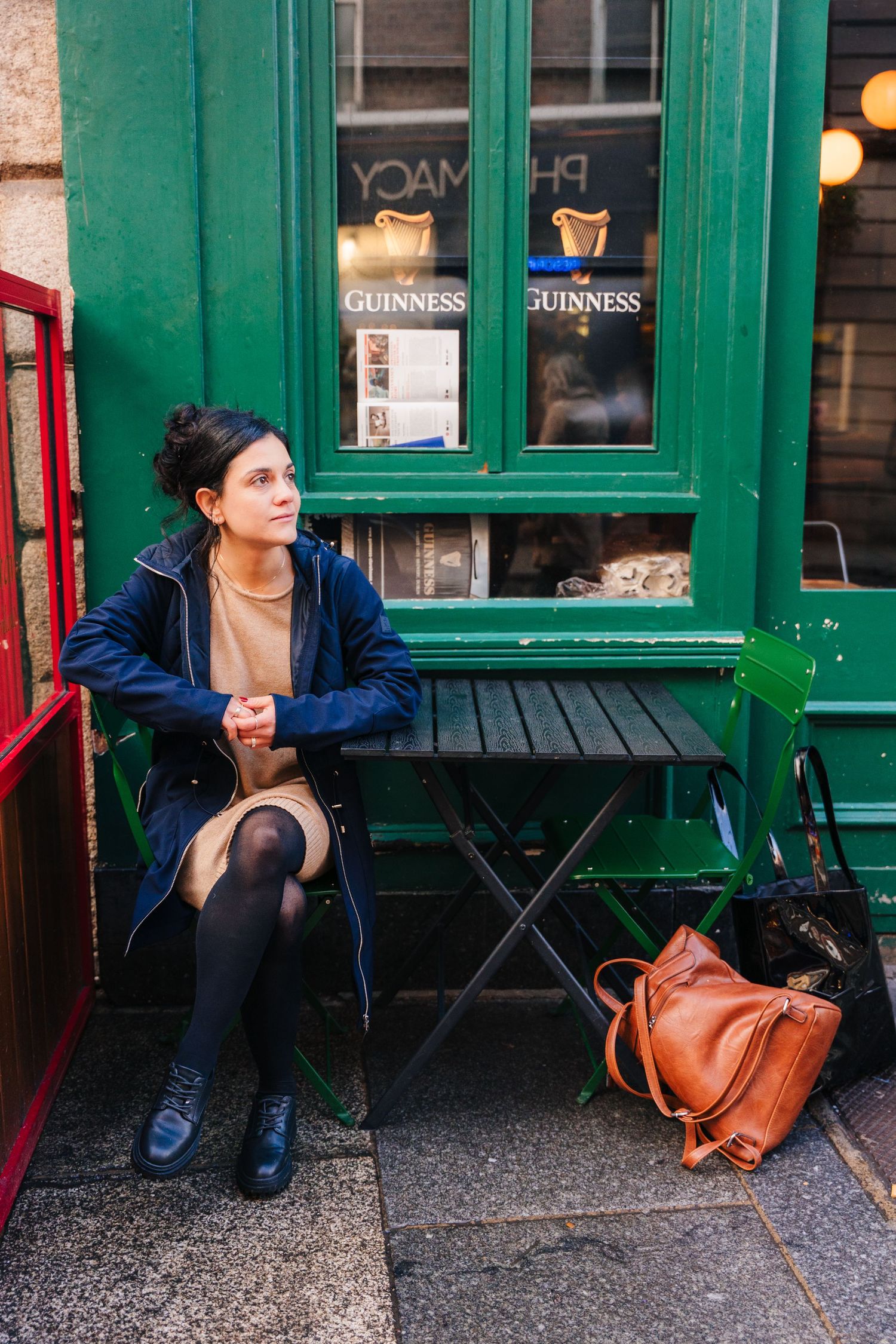 A person sits on a bench outside a traditional Irish pub with green trim and Guinness signs in the window. professional headshots dublin