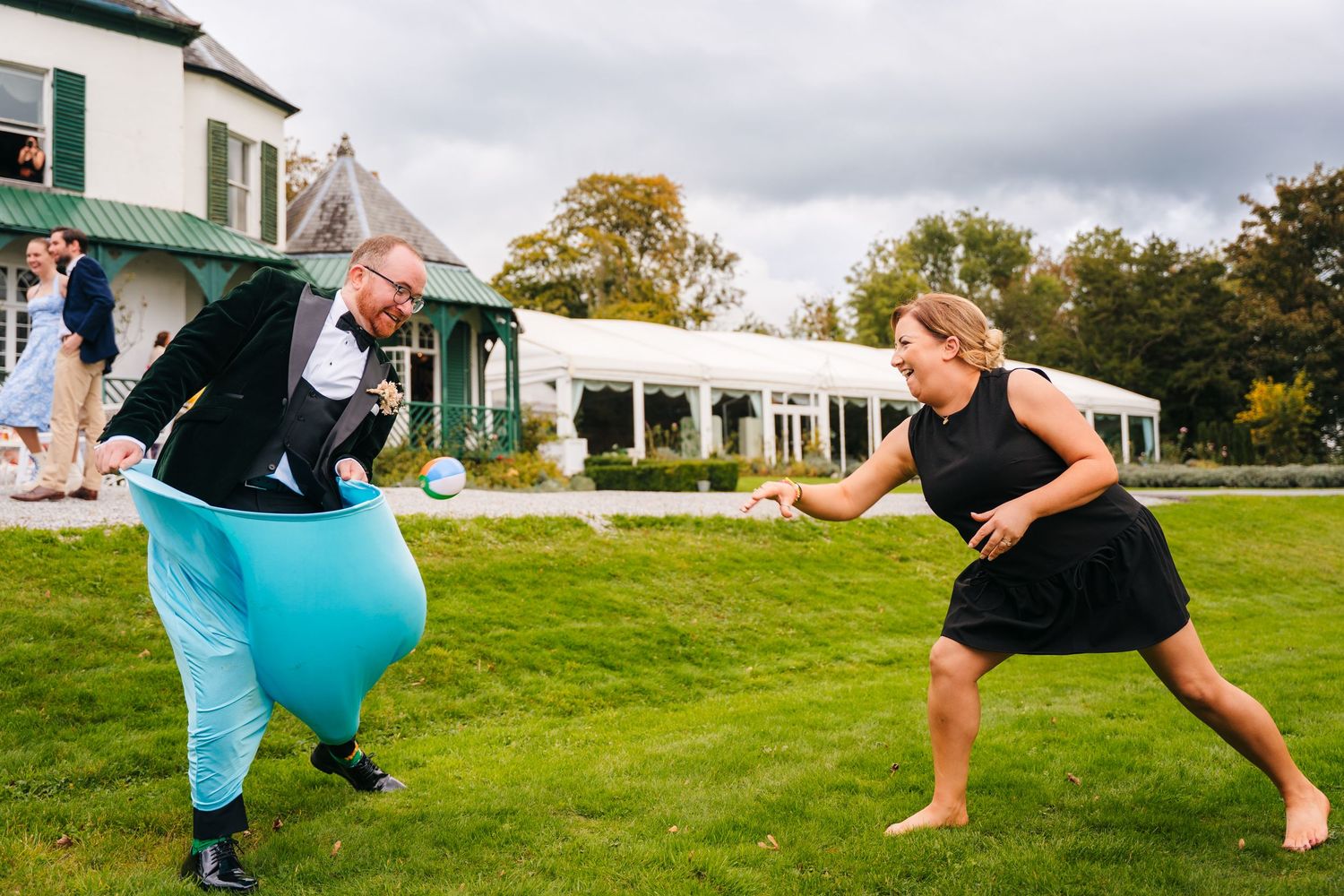 Two people engage in a playful dance battle outdoors on a lawn with a white building and tent in the background. Wedding photographer Dublin