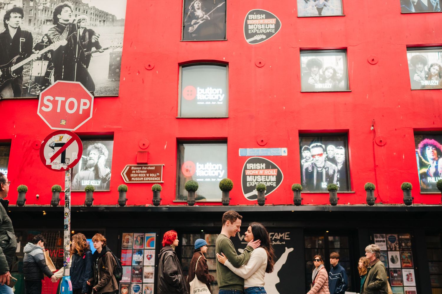 A crowd gathers in front of a vibrant red wall decorated with vintage black and white photographs. Surprise proposal dublin photography