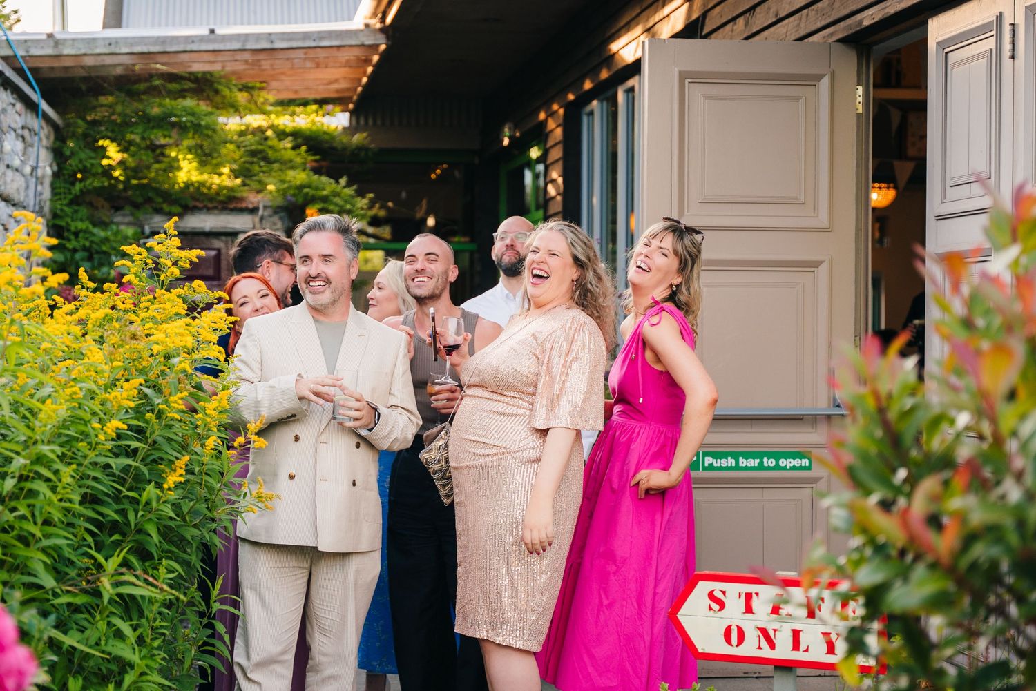 Wedding party gathered outdoors on a porch with bright pink and floral summer dresses. . Village Barn Tyrrellspass wedding photographer Irel