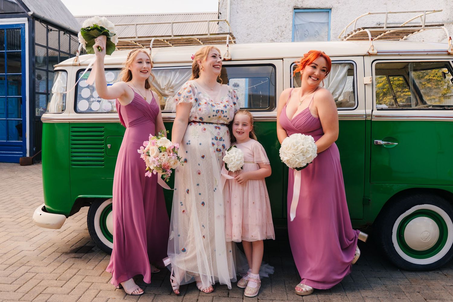 A vintage green VW bus serves as a backdrop for a wedding party gathering outside a white building. . Village Barn Tyrrellspass wedding phot