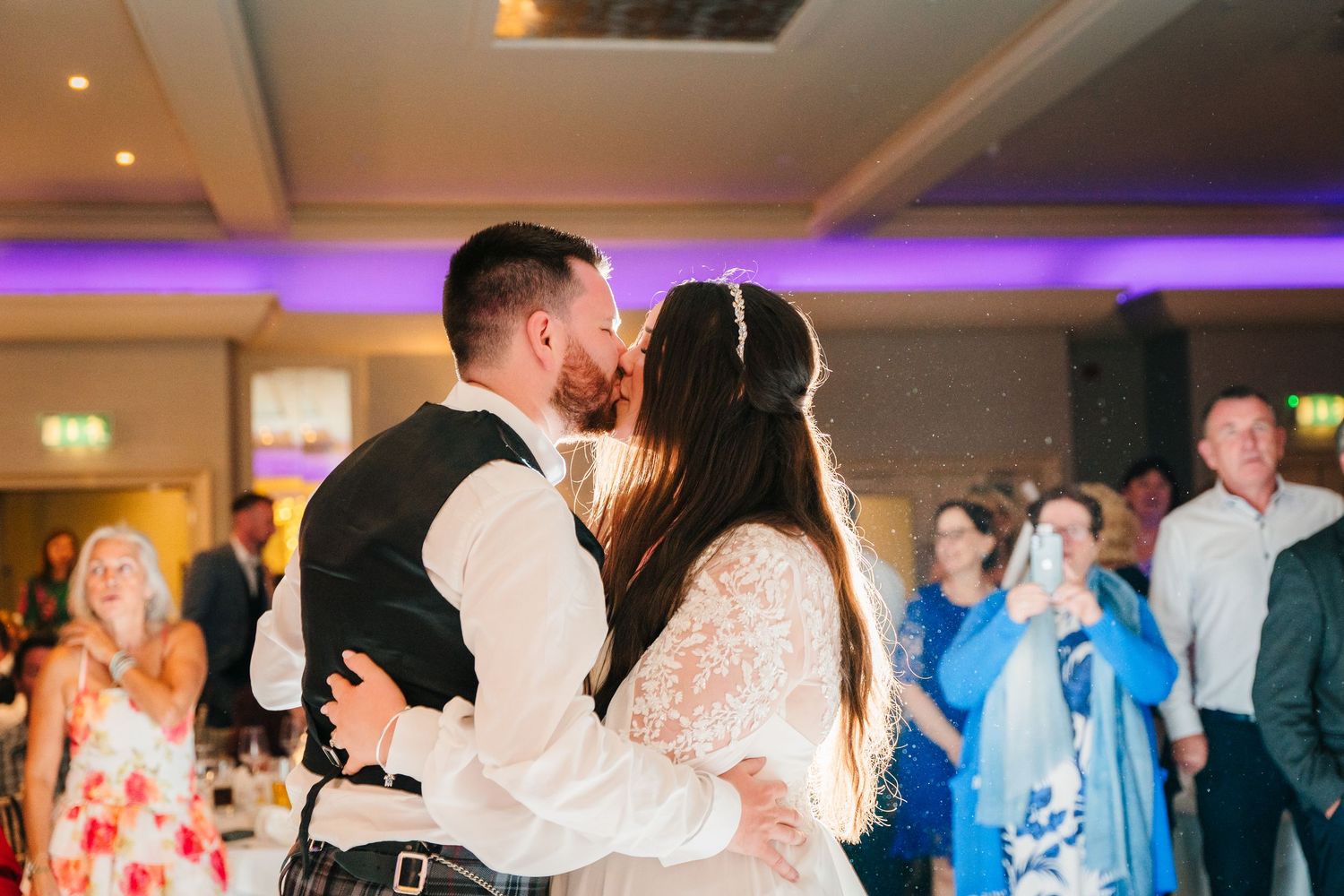 Couple sharing their first dance at wedding reception with purple lighting and guests watching. Portmarnock Hotel Wedding PHOTOGRAPHER Dubli