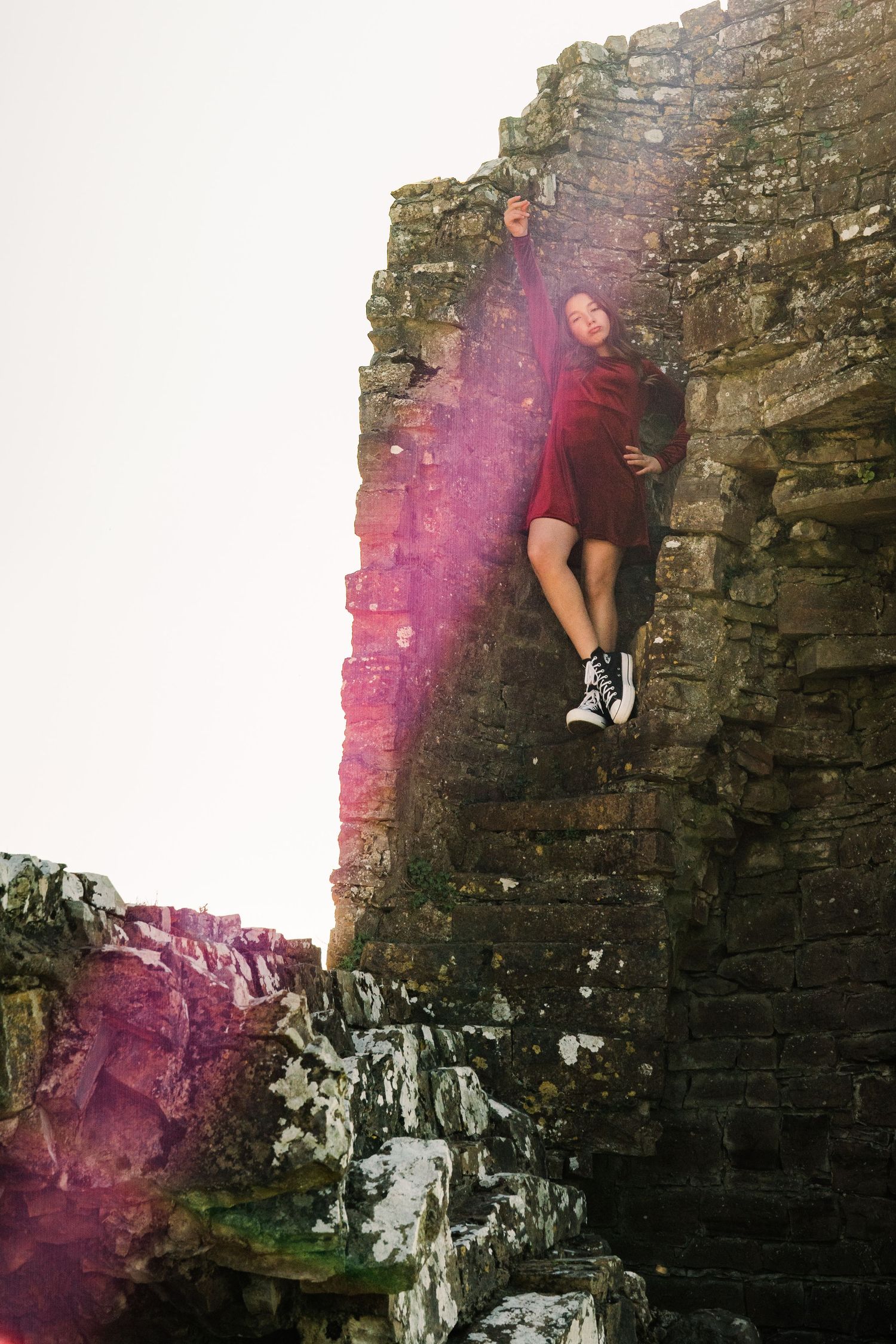Figure in red dress poses against stone castle wall with artistic lens flare effect. Family PHOTOGRAPHER Dublin
