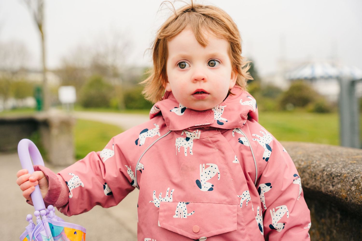 Small child wearing a pink patterned winter coat with dalmatian print design stands outdoors on a cloudy day. PHOTOGRAPHER Dublin