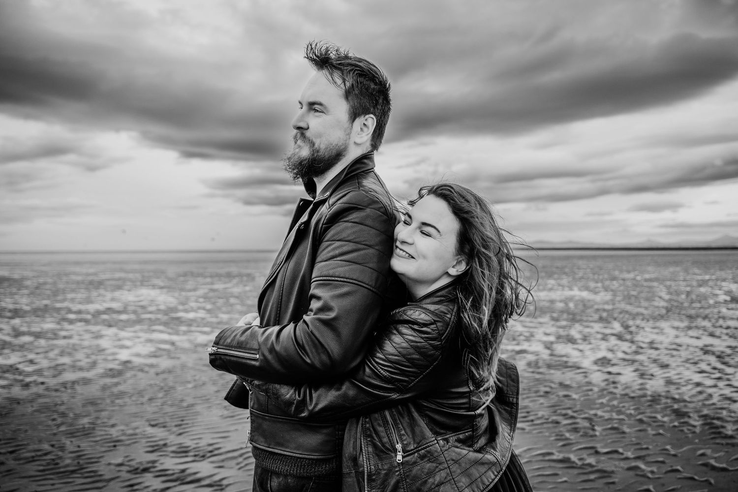 Couple shares an intimate moment together on a rocky beach under dramatic storm clouds. engagement PHOTOGRAPHER Dublin