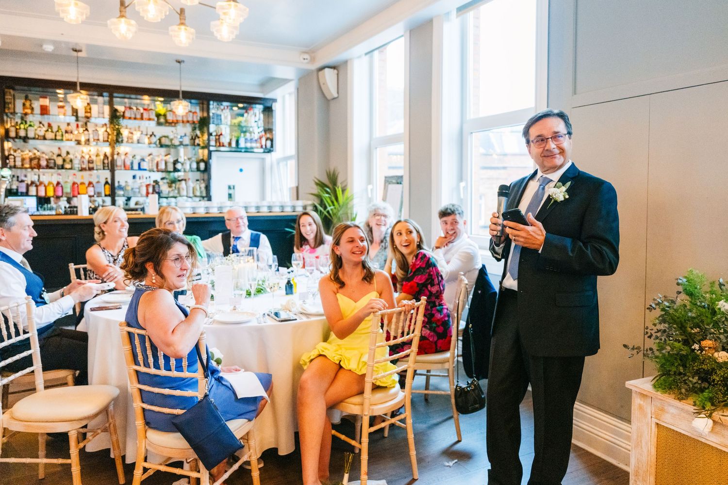Wedding reception guests gather in bright indoor venue with bar and white decor. PHOTOGRAPHER Dublin Ireland Wedding