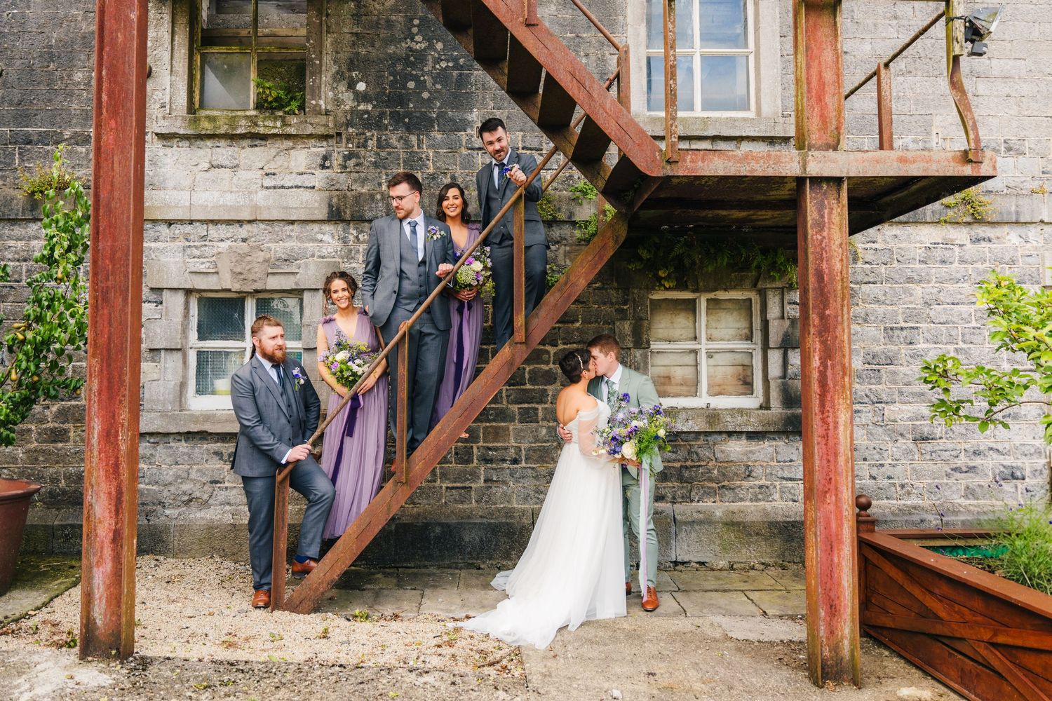 Millhouse slane wedding photographer dublin Wedding party poses on rustic wooden stairs against stone building exterior.