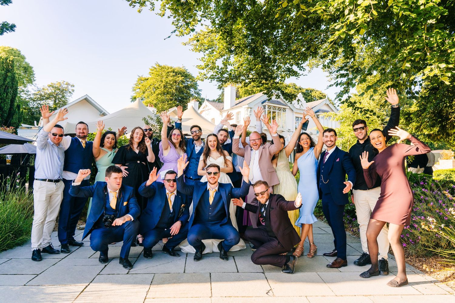 Poulaphouca Wedding photographer wicklow  Large wedding party group poses together outdoors on a sunny day with trees in background.