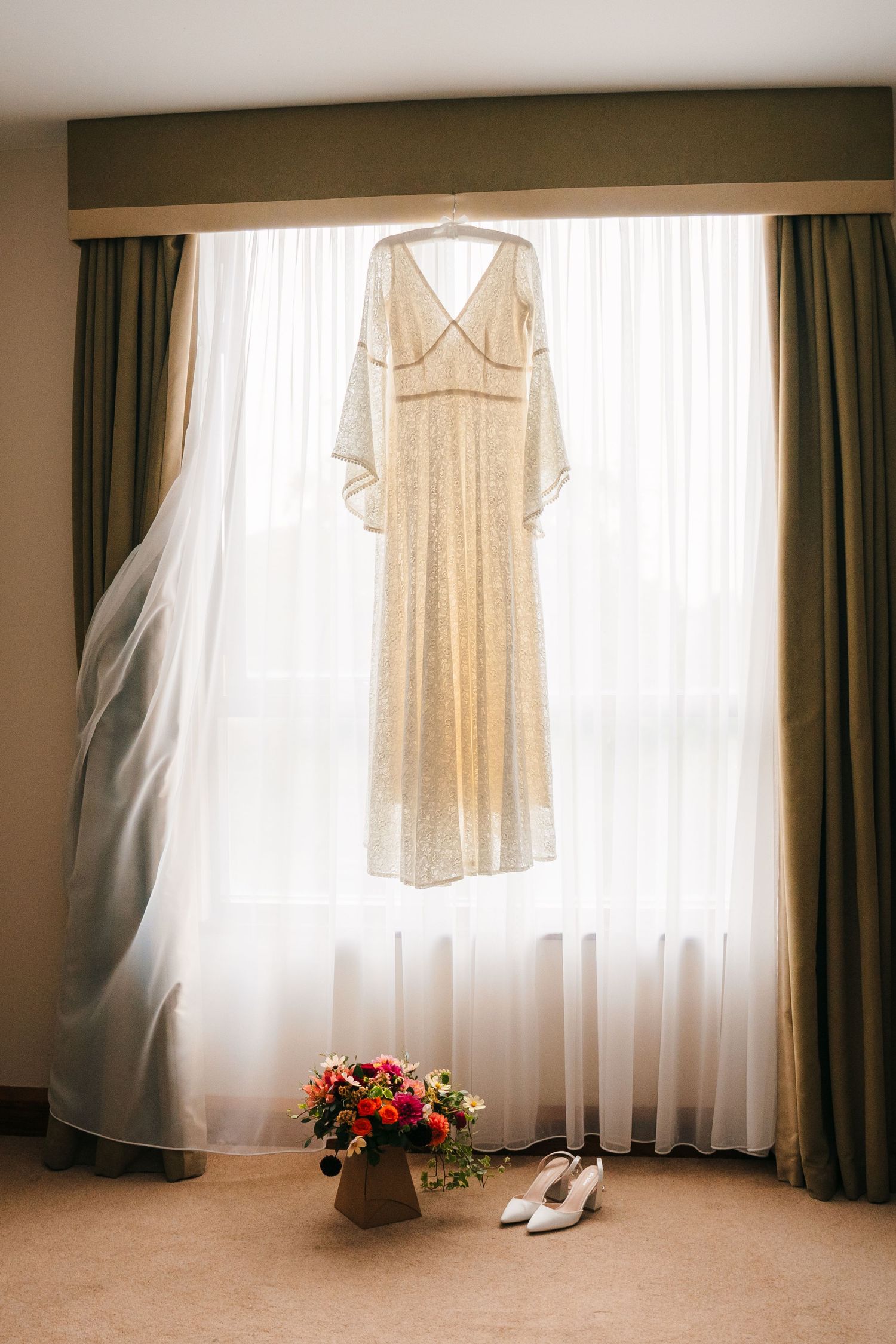 Cream colored wedding dress hanging in window with white veil and floral arrangement beneath. Wedding Photography Trim Castle Ireland