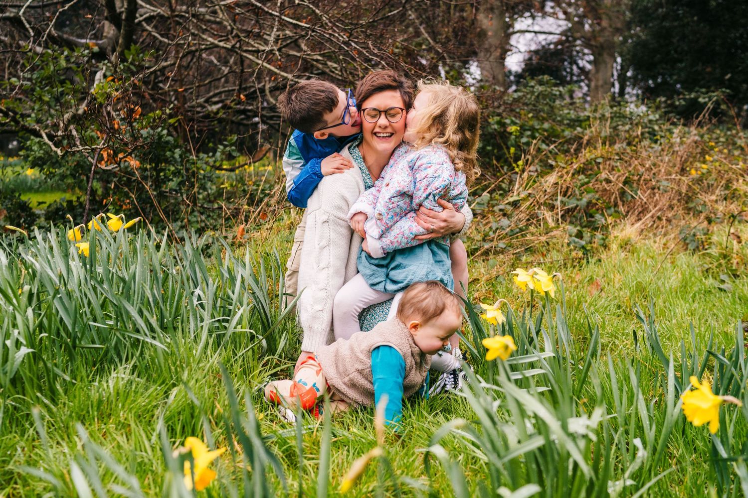 A group sits together in a spring garden with blooming yellow daffodils surrounding them on a grassy slope.Family photographer Dublin Irelan