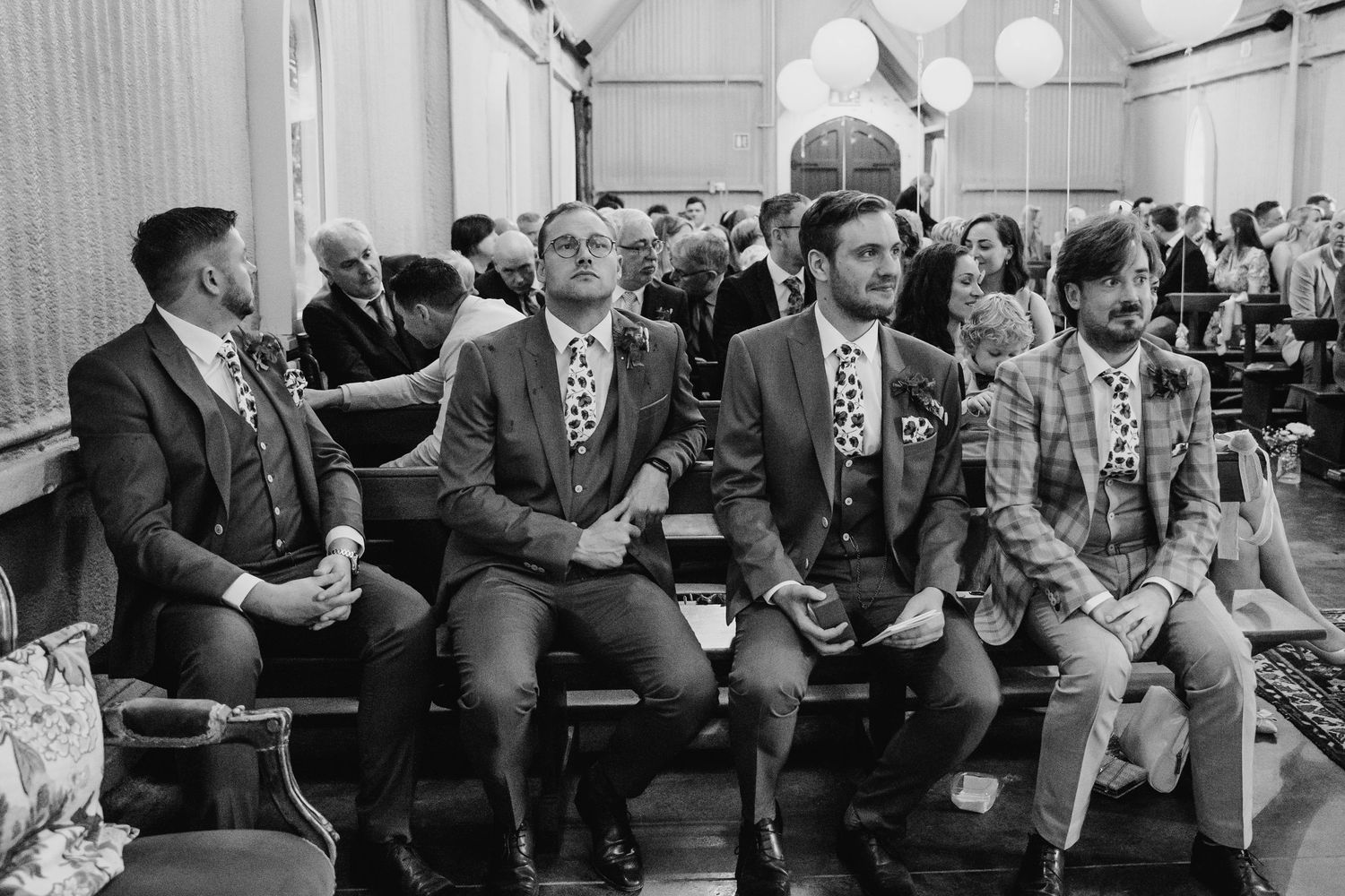 Wedding guests in suits sit in a row during a ceremony in a vintage black and white photograph. Wedding photographer Dublin