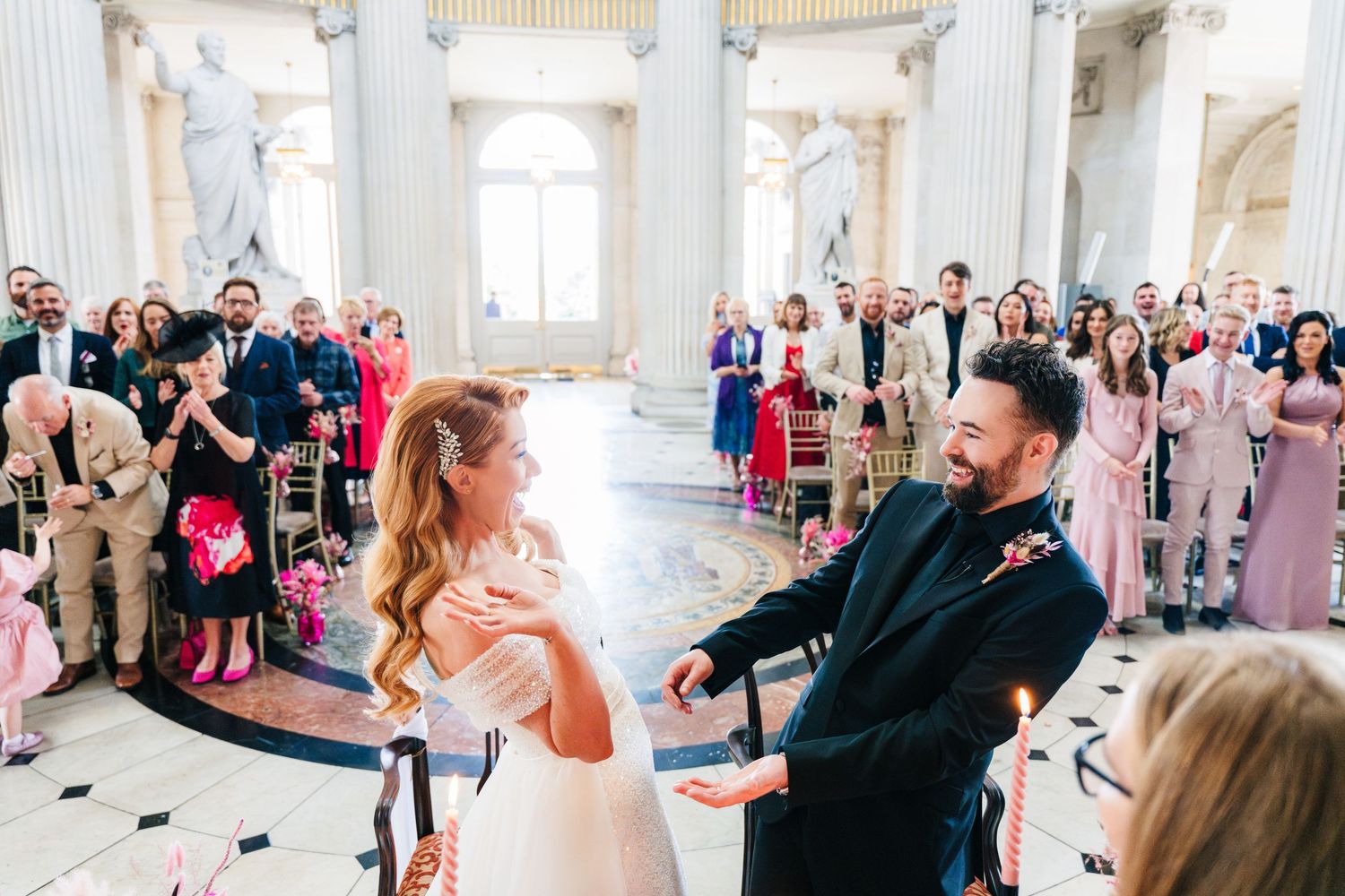 Couple shares a joyful dance moment in a grand columned hall with wedding guests looking on.  city hall dublin wedding photos