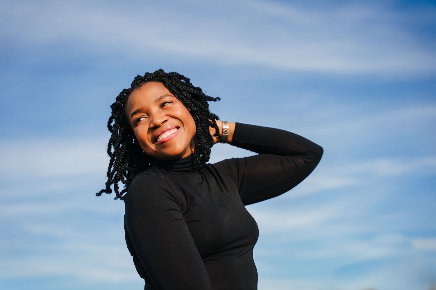 Someone wearing a black sweater poses against a bright blue sky with clouds Professional headshots PHOTOGRAPHER Dublin