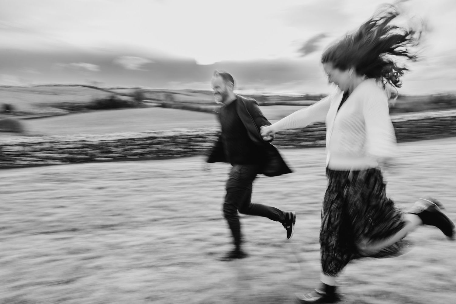 Two people running along a beach in black and white with motion blur creating a dynamic sense of movement and energy. PHOTOGRAPHER Dublin ir