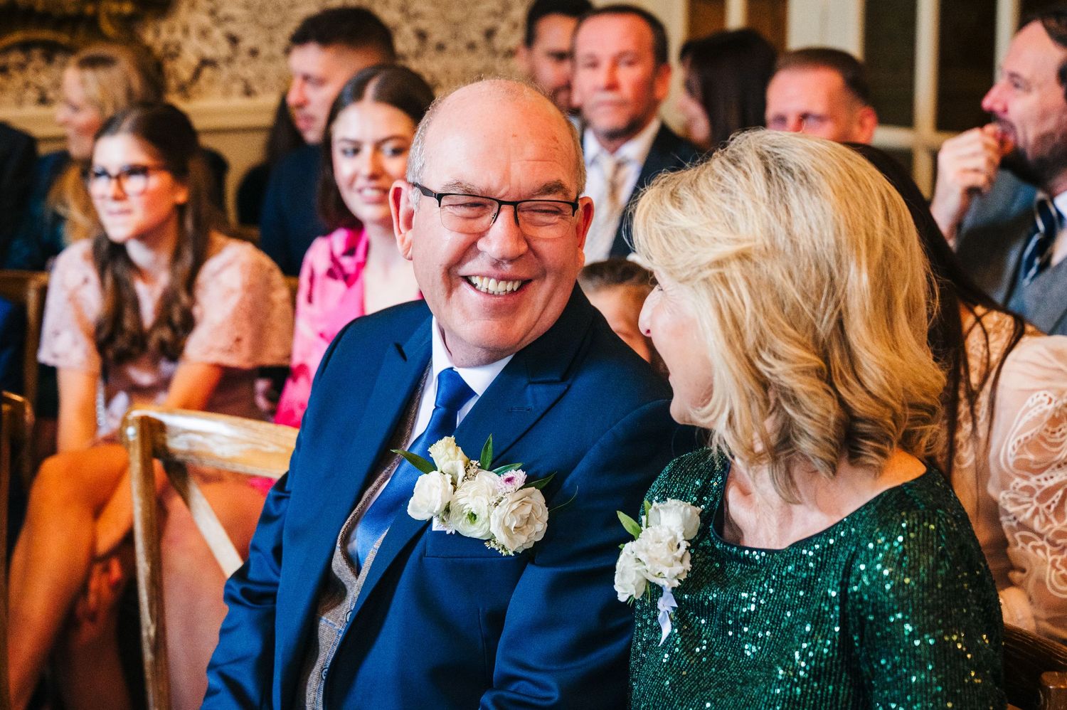 Wedding guests in formal attire share a candid laughing moment in an ornate reception room.  Virginia Park Lodge Wedding Photographer Cavan