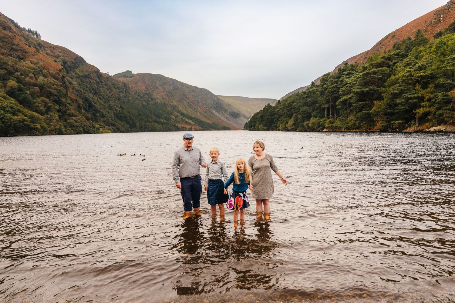 A panoramic view of a family standing together at the edge of a scenic mountain lake.Family photogrAPHER DUBLIN