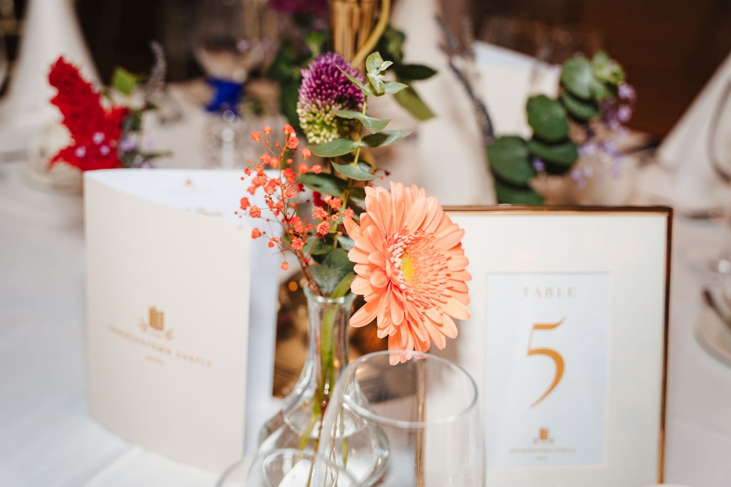 Wedding reception table setting with peach gerbera daisy centerpiece and gold table number card.