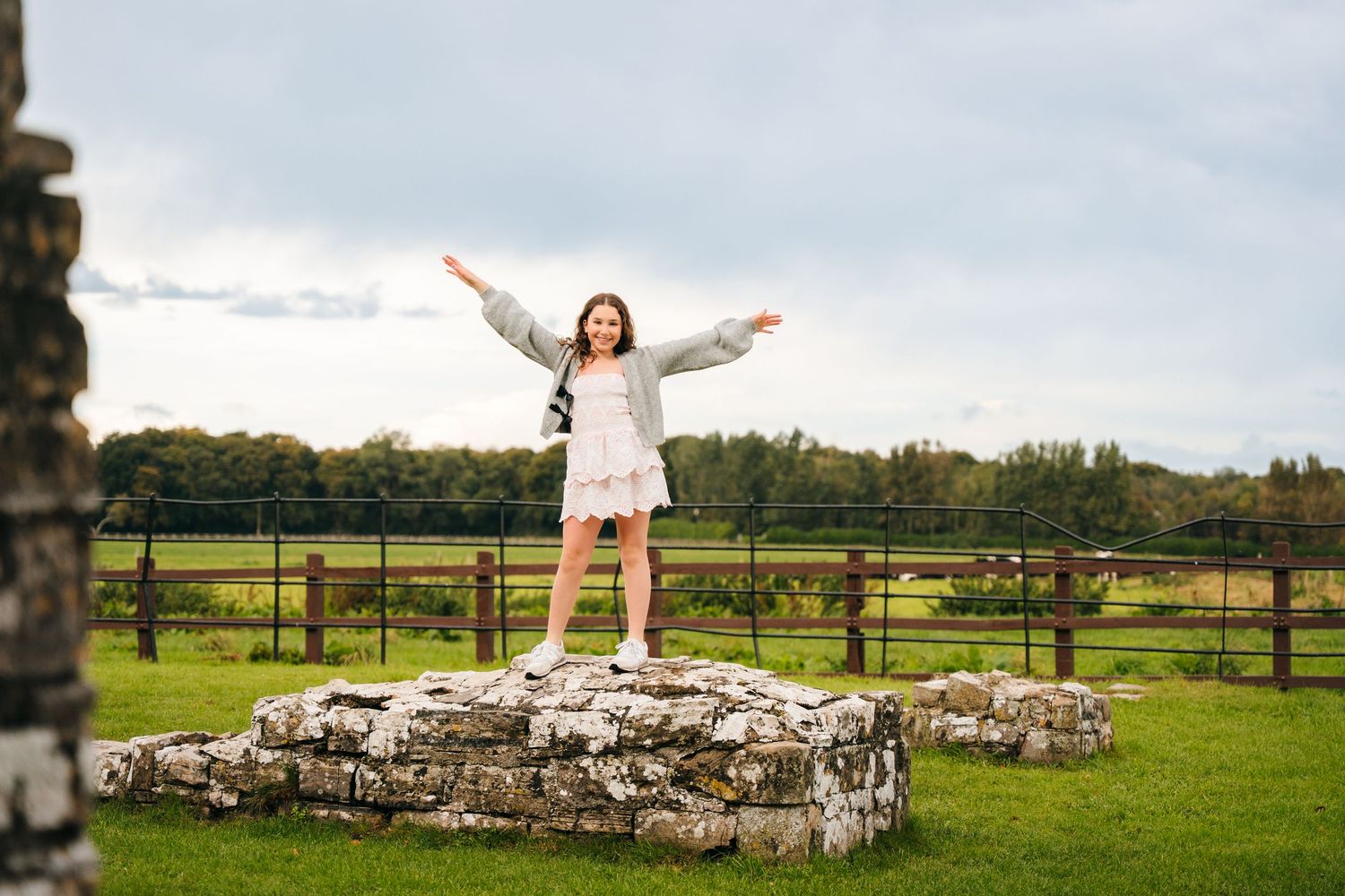 Person with outstretched arms stands among ancient stone ruins in a green pastoral landscape. BEctive abbey family photographer dublin