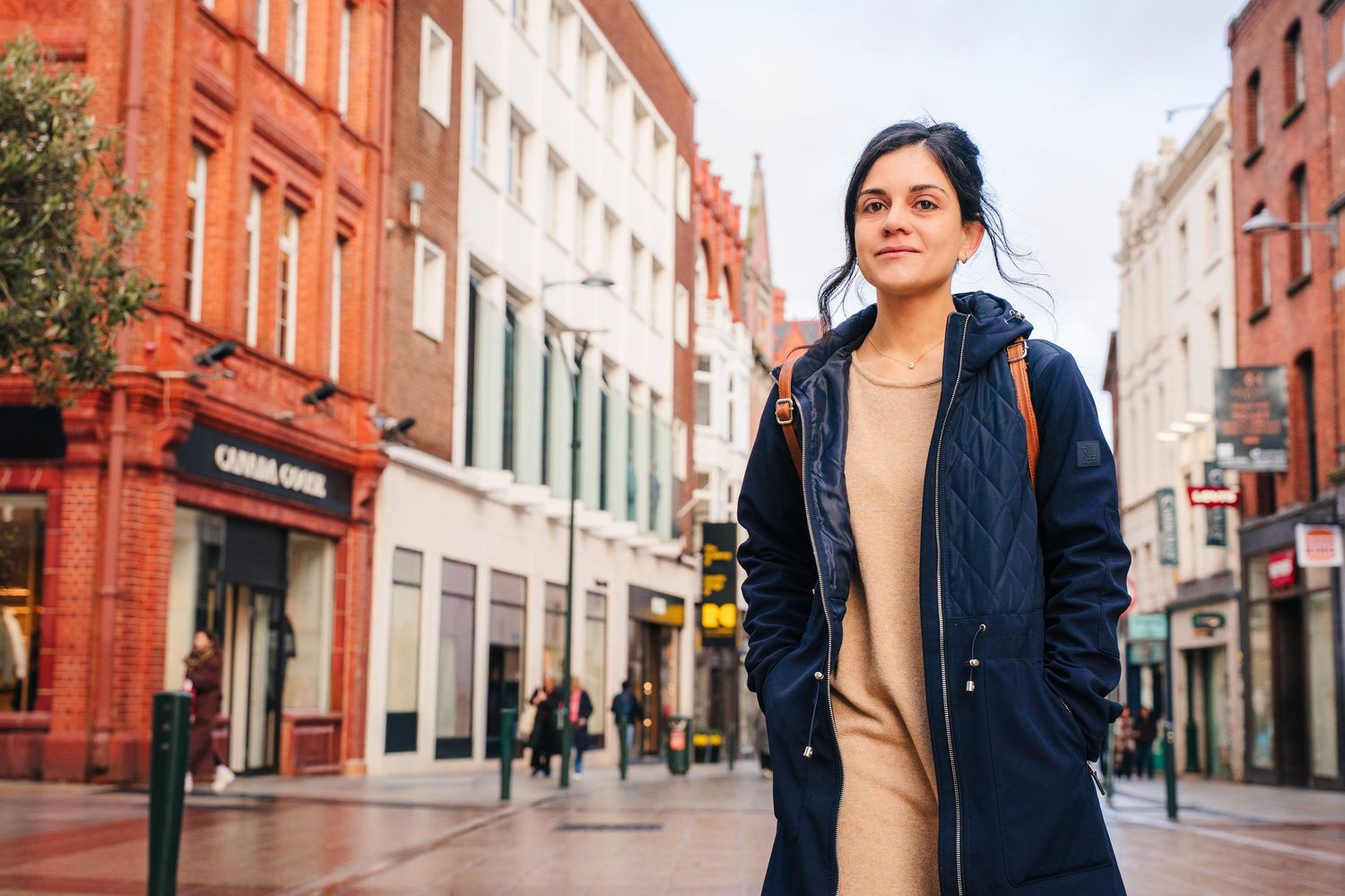 Person in navy blue coat and beige sweater walking through historic brick buildings on city street. professional headshots dublin