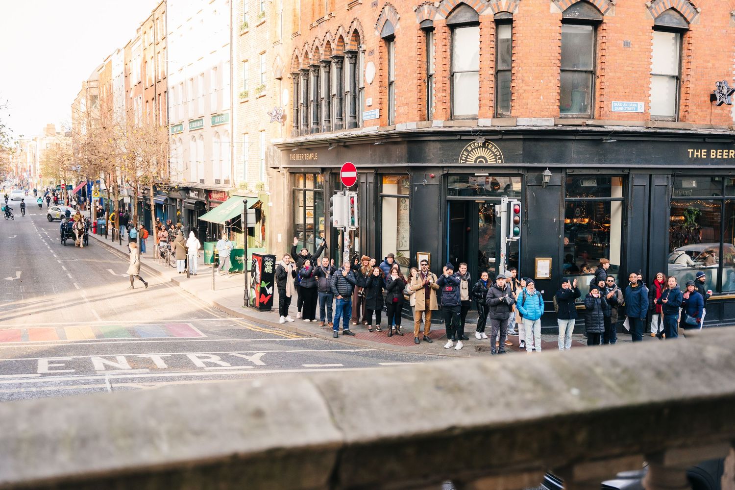 Large crowd gathers outside historic brick building on city street. Wedding photographer dublin