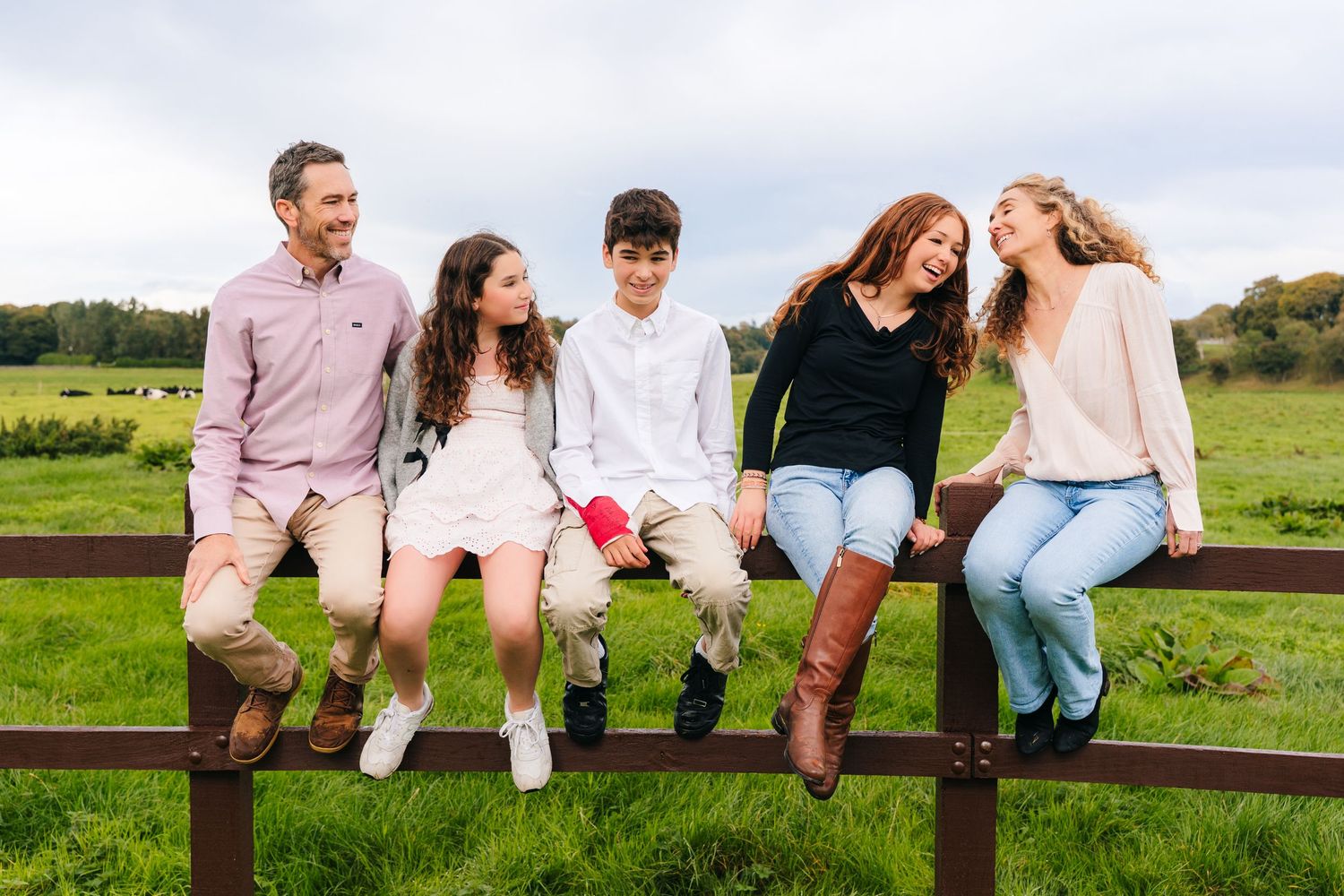 Family members sit casually on a wooden fence in coordinated outfits during an outdoor photo session. Family photographer dublin