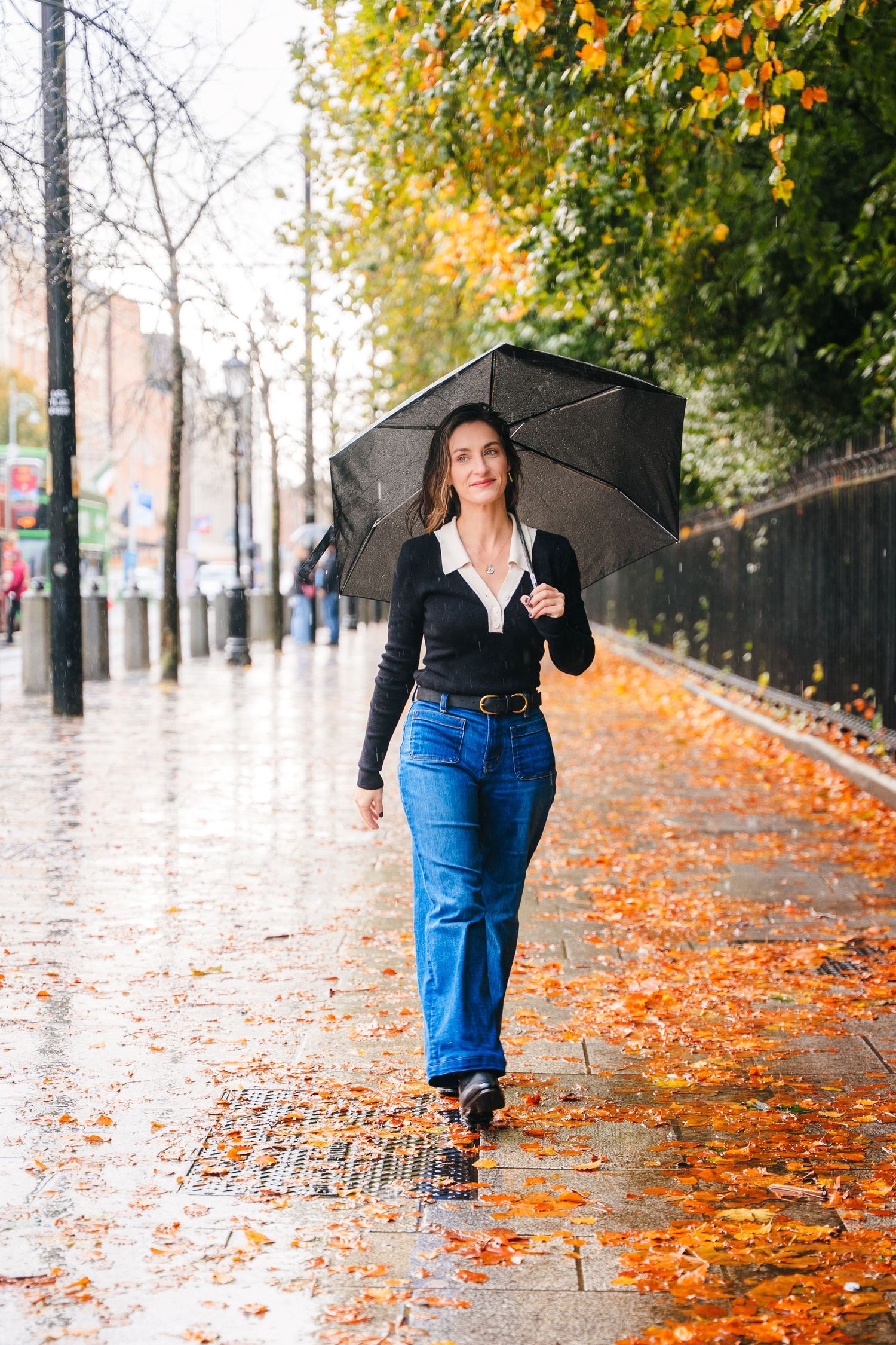 Autumn street scene with person holding umbrella walking through fallen orange leaves. professional headshots dublin photographer
