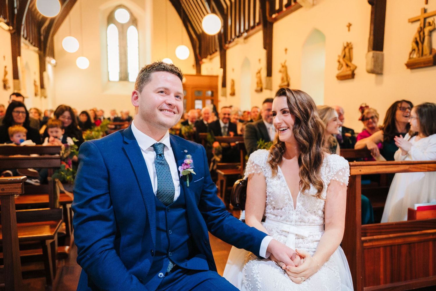 Wedding ceremony taking place in a beautiful church with arched windows and wooden pews.