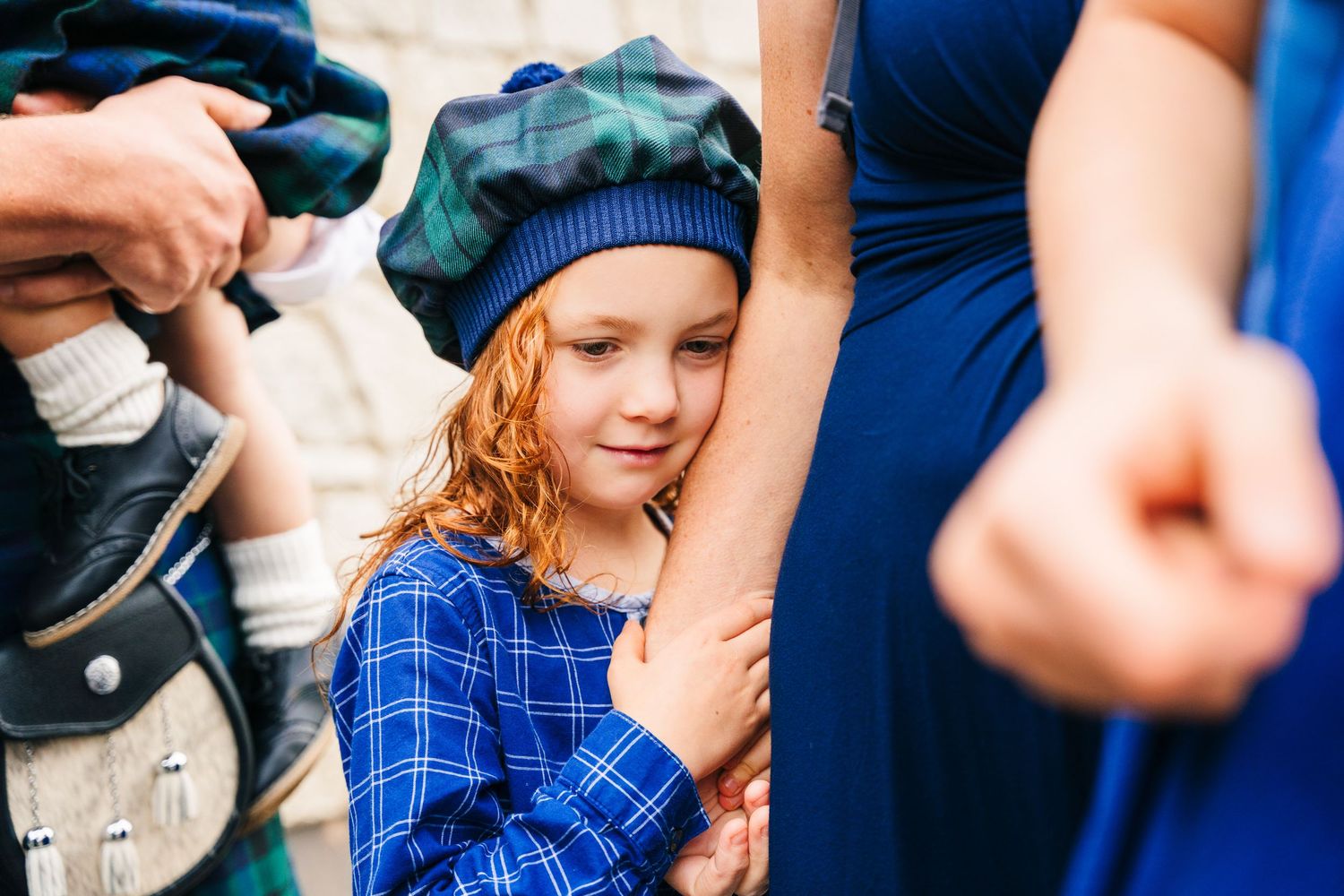 A person in blue plaid holds a small white object while others gather around in a blurred background. Family photogrAPHER DUBLIN