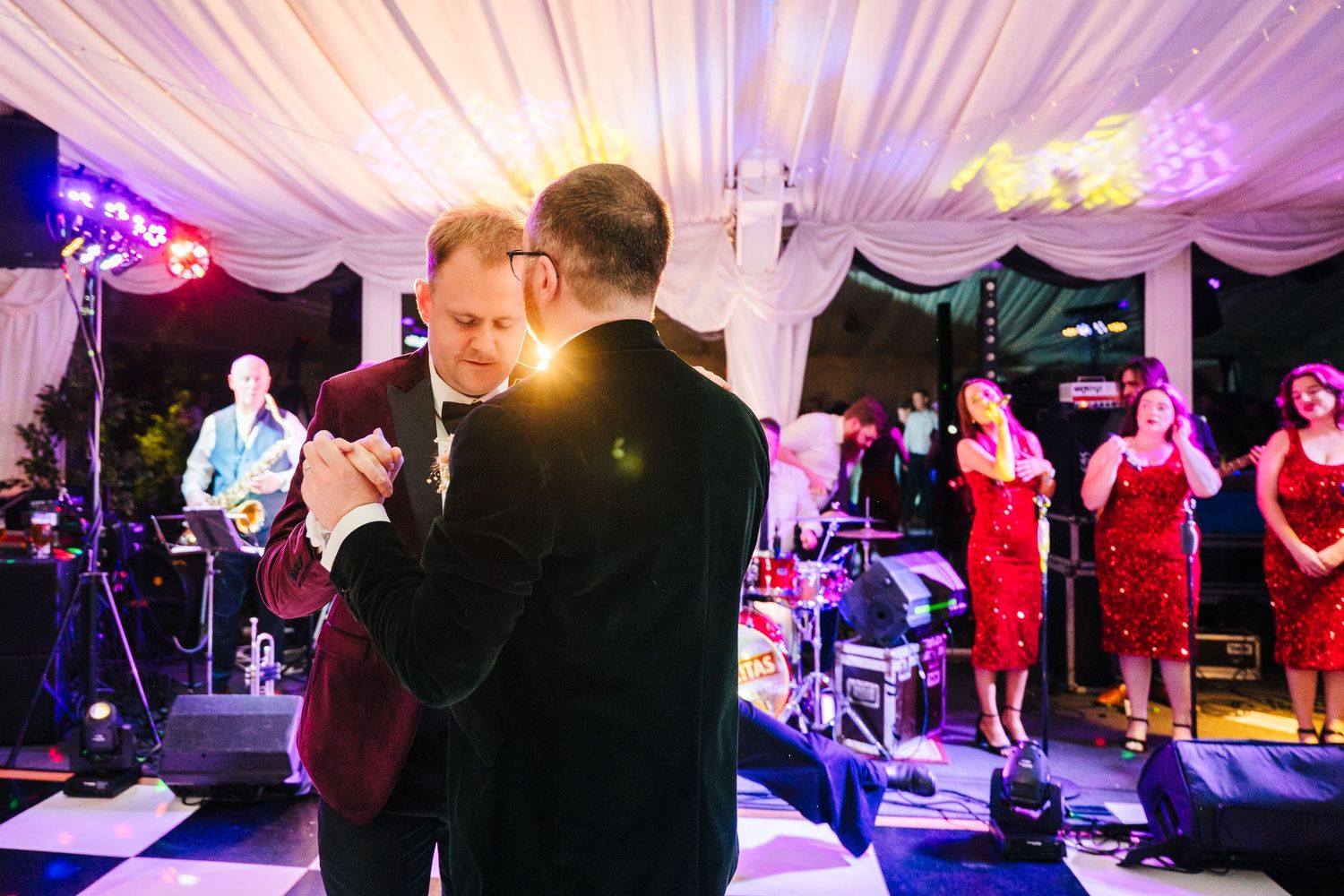 A couple dances under purple-lit tent with a live band performing in the background. LGBTQ Ashley Park Wedding Photographer