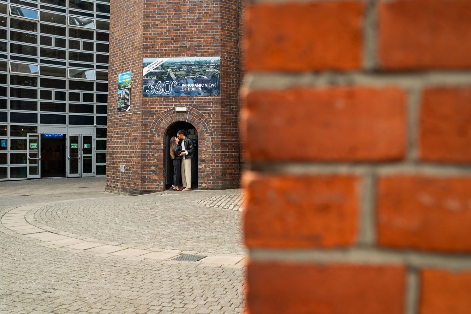 Red brick industrial-style architecture with metal grating and curved walkway creates a modern urban aesthetic. Couple's Photoshoot PHOTOGRA