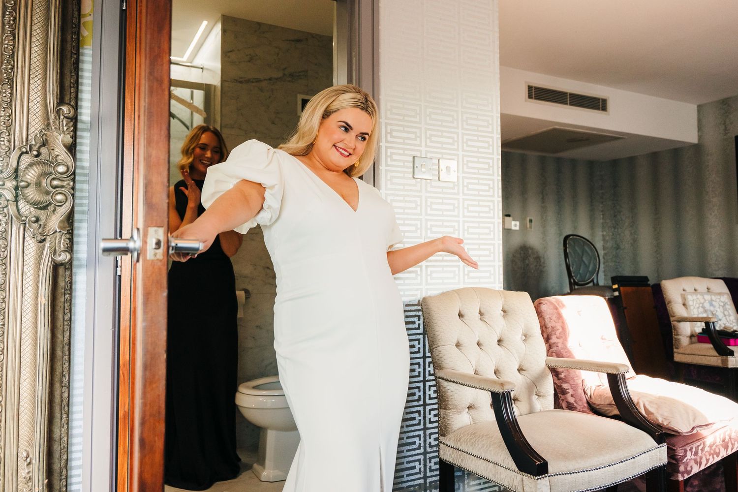 Bride and bridesmaids laughing together during wedding day preparations in an elegant hotel room. Wedding photographer dublin