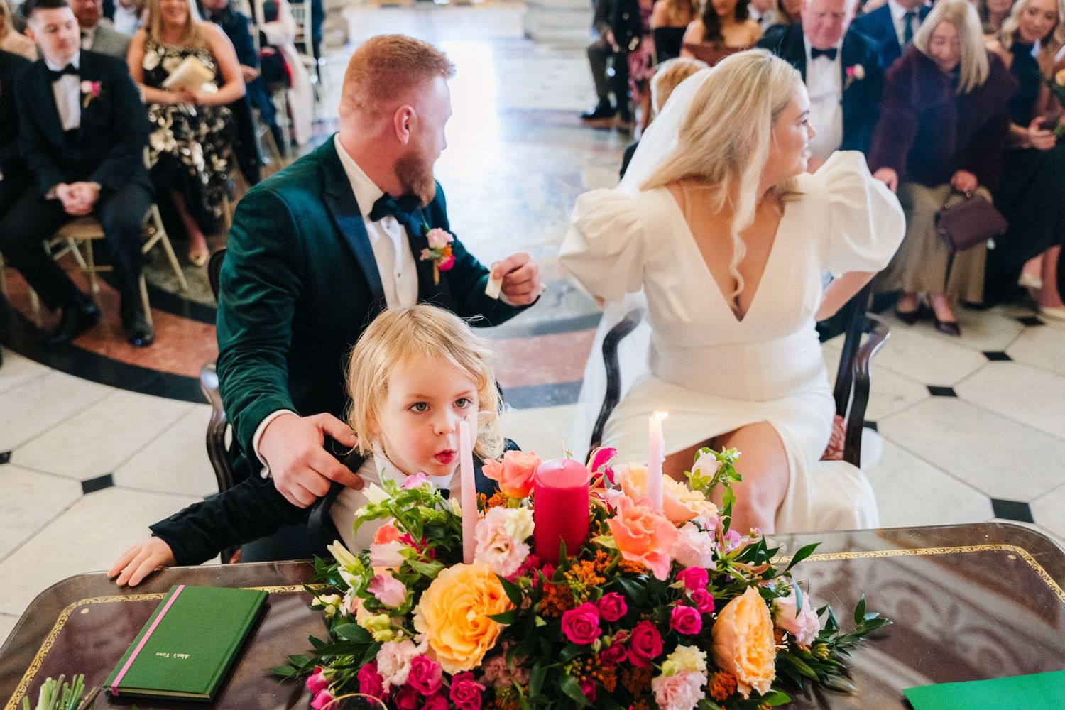 Wedding couple and child at reception with colorful floral centerpiece on checkered floor. Wedding photographer dublin