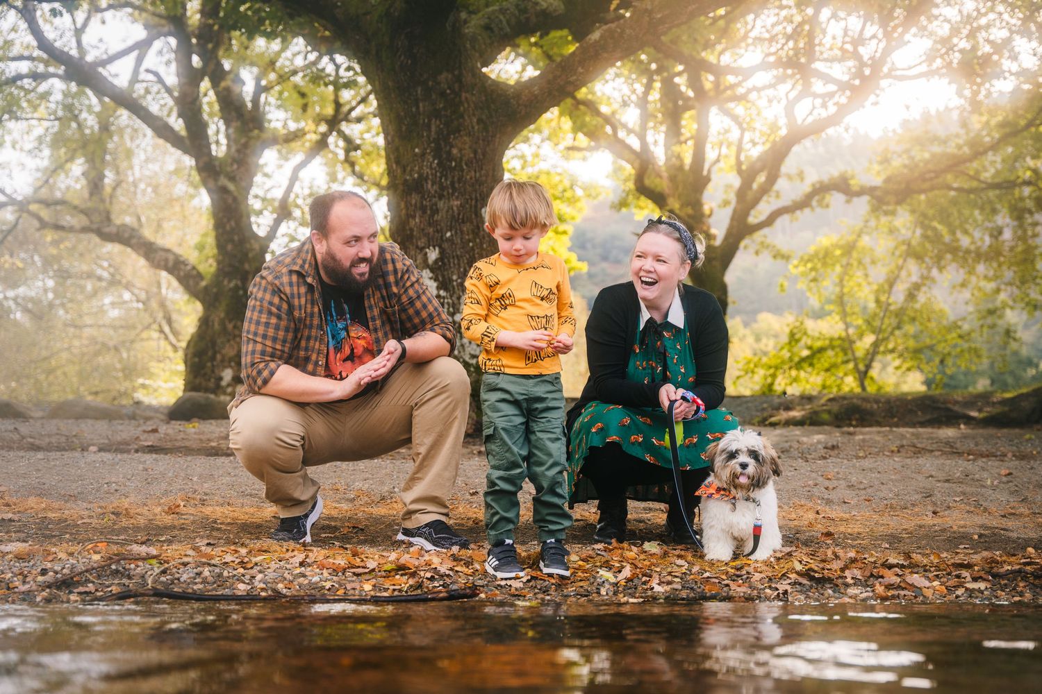 A family enjoying an autumn day by a stream with their small white dog in a golden-lit park setting. family PHOTOGRAPHER Dublin