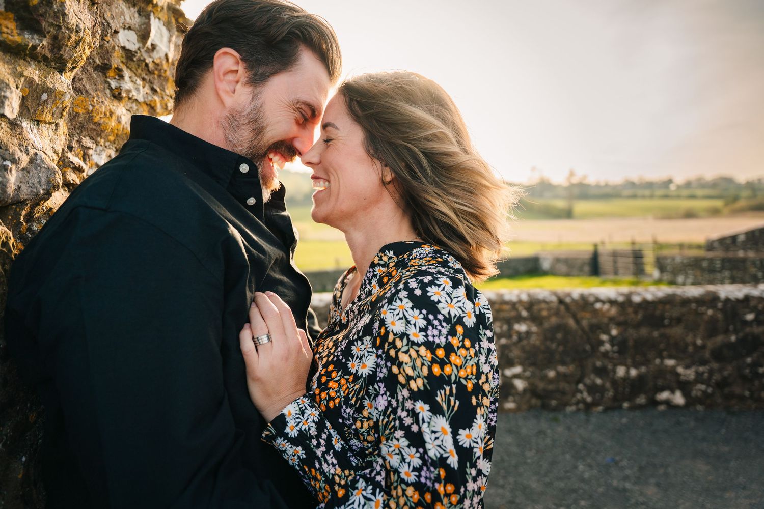 Romantic couple sharing intimate moment against stone wall in countryside with fields in background. PHOTOGRAPHER Dublin ireland