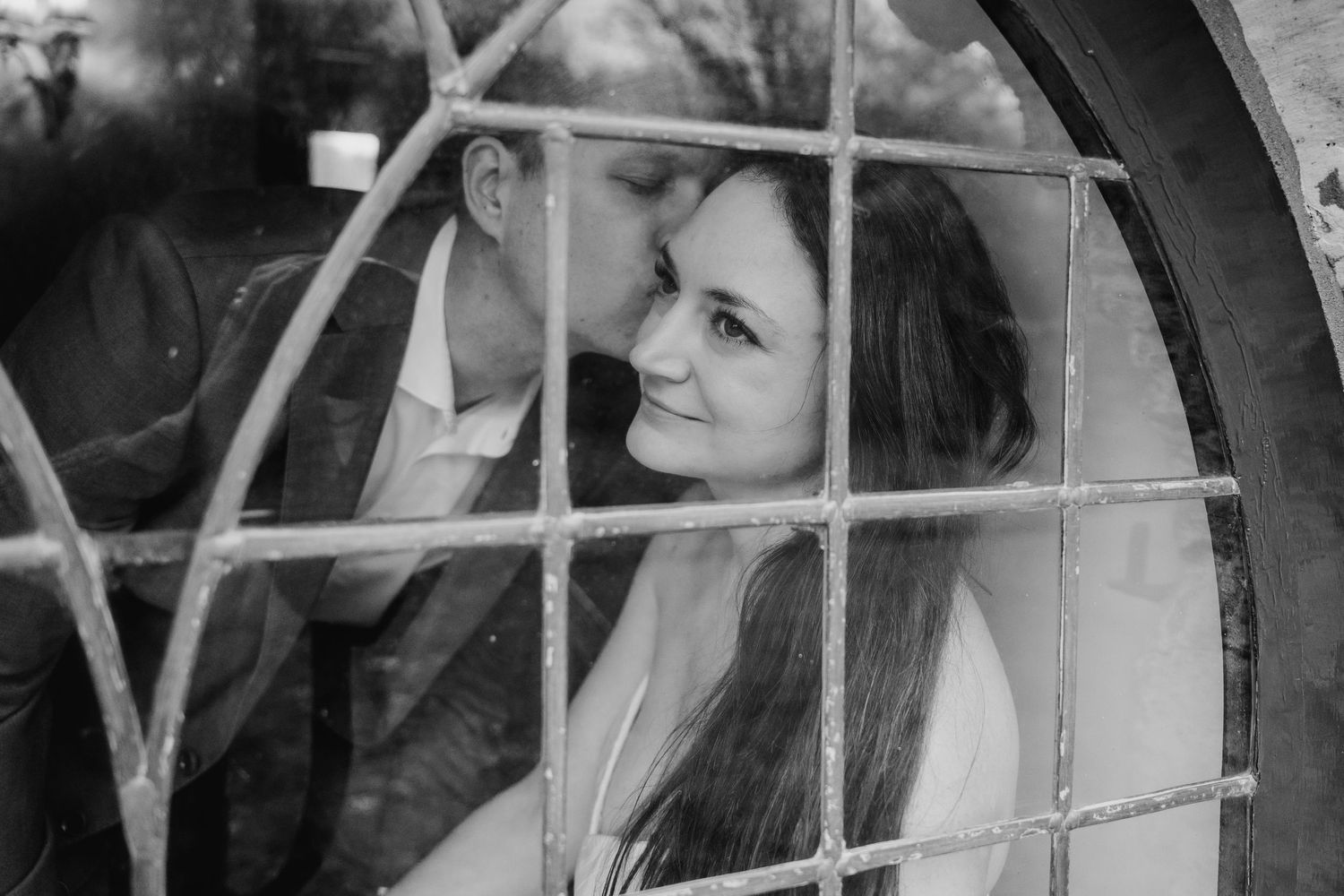 A black and white romantic shot through a window frame of a couple gazing at each other on their wedding day. PHOTOGRAPHER Dublin ireland
