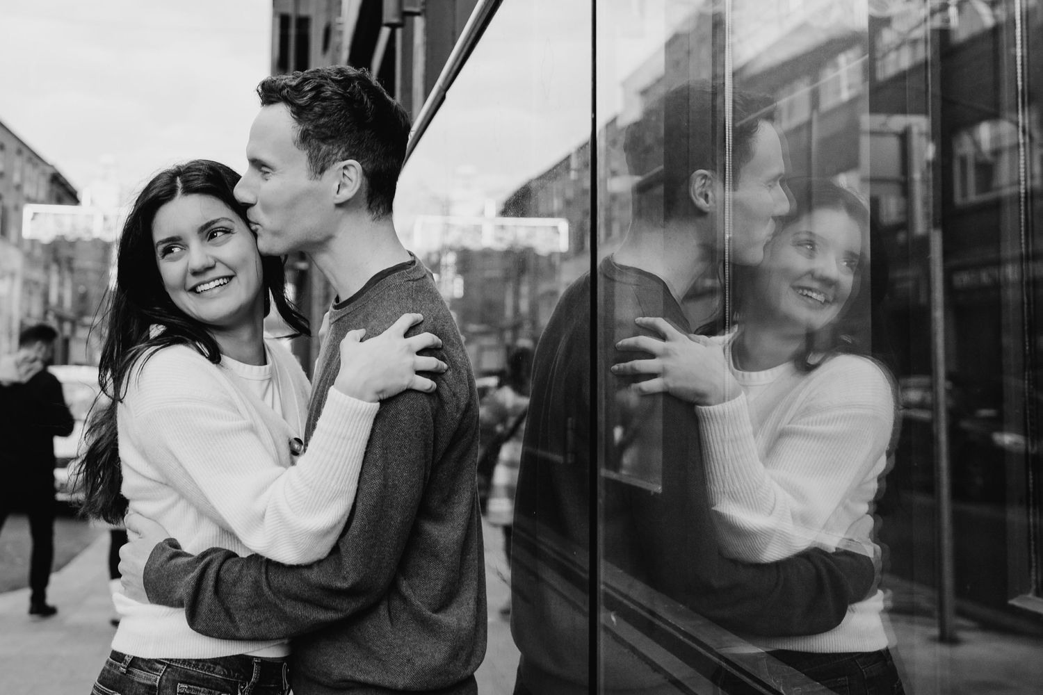 A romantic black and white photograph showing a joyful couple embracing against a storefront window reflection. PHOTOGRAPHER Dublin PHOTOGRA