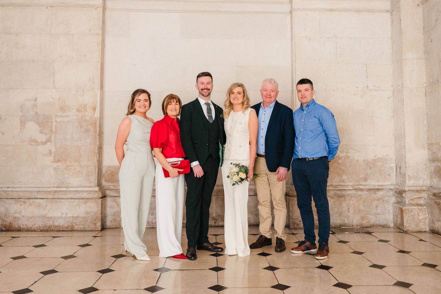 Group photograph taken inside historic Dublin building with white stone walls and architectural details. City Hall Dublin wedding photogrAPh