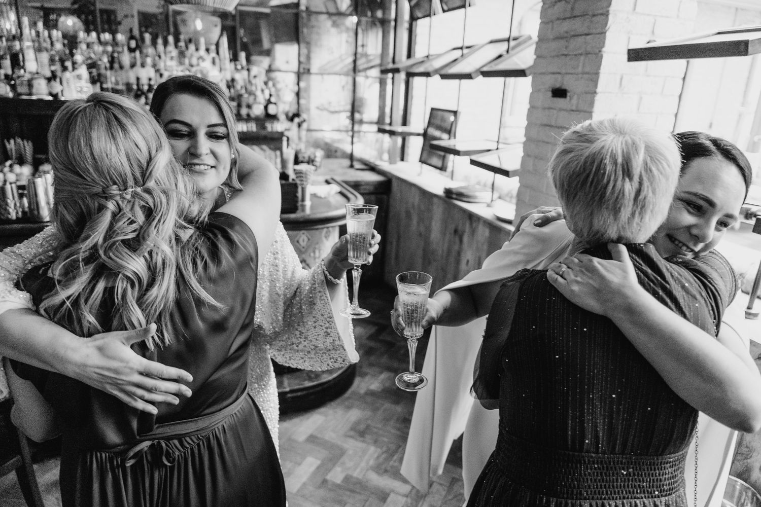 Black and white candid photo of celebratory hugs at a bar gathering. House Dublin Wedding Photographer