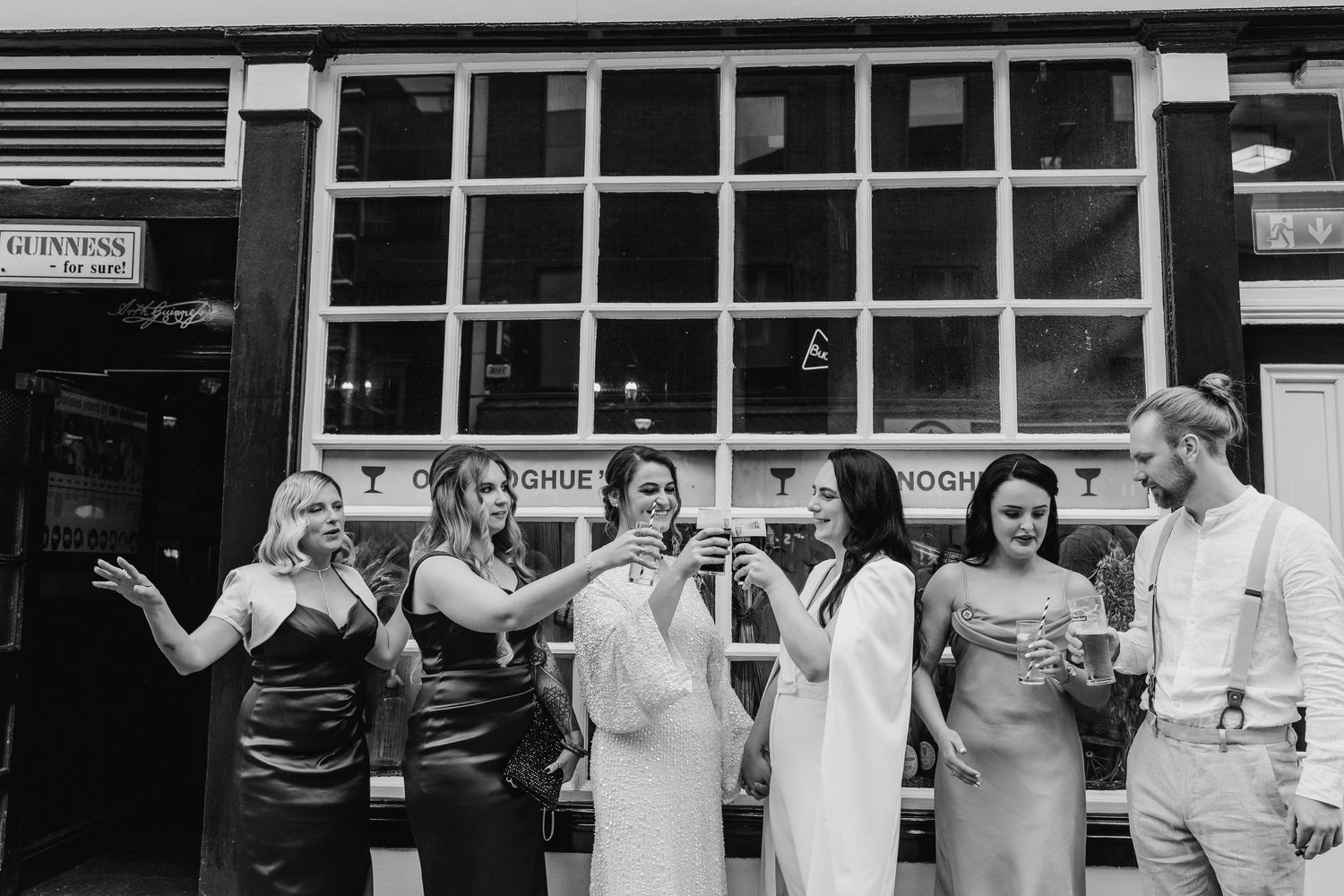 Group poses together outside a building with gridded windows for a casual black and white photo. House Dublin Wedding Photographer