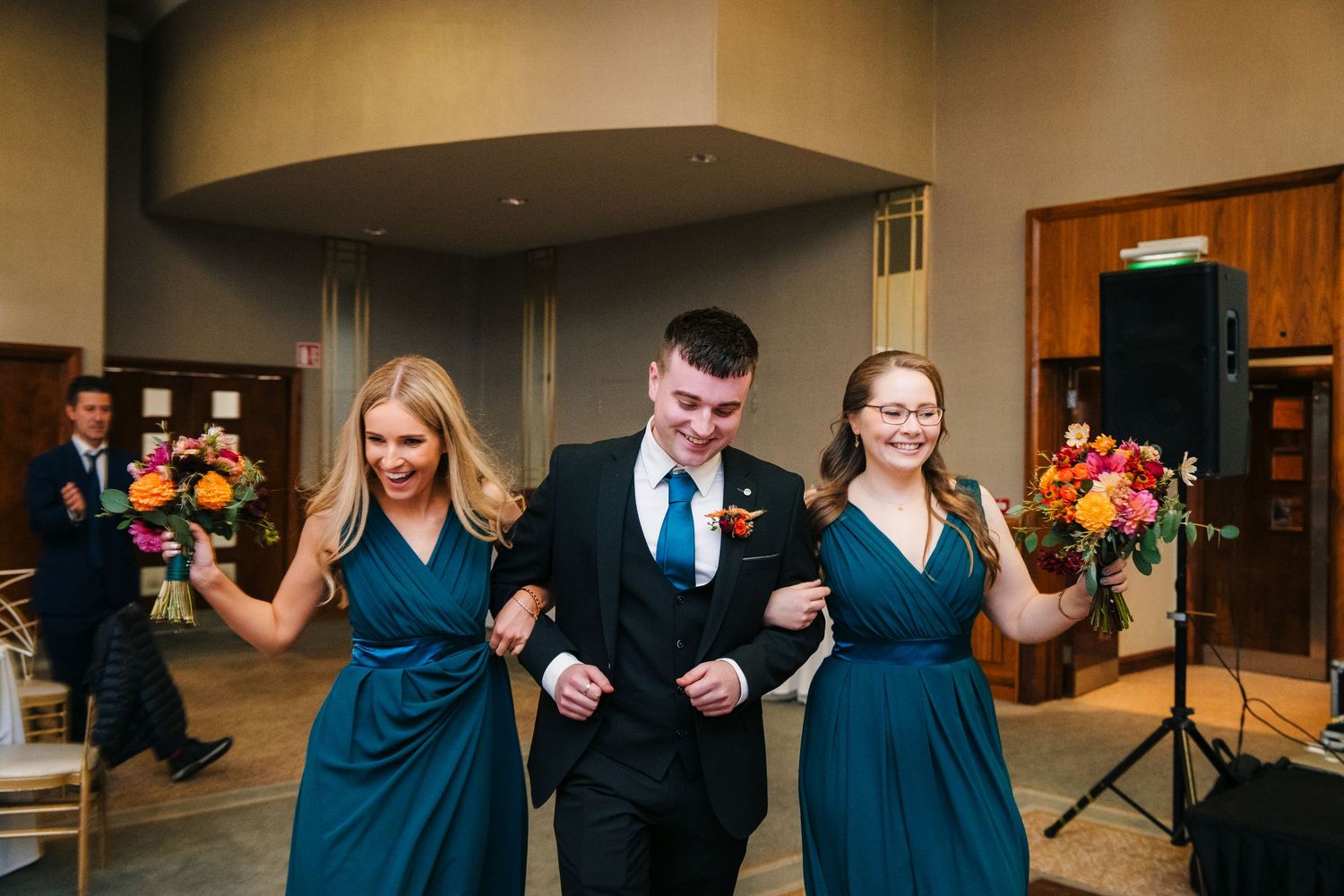 Wedding party members in matching teal dresses and formal attire walk arm in arm while holding colorful bouquets.Wedding Photography Trim Ca