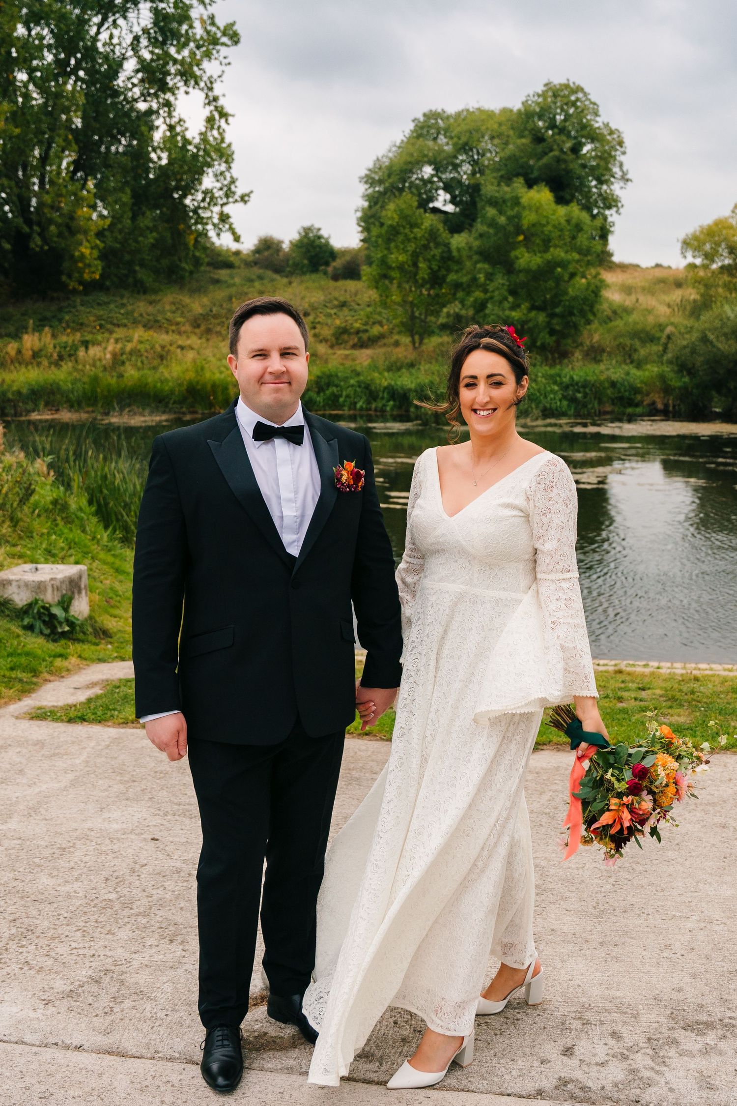 Newlyweds in formal attire pose by a serene pond on their wedding day. Wedding Photography Trim Castle Ireland