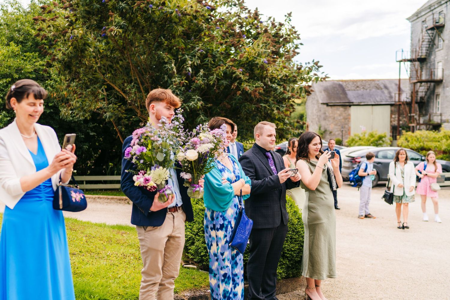 Millhouse slane wedding photographer dublin Wedding guests mingling outdoors on a sunny day with church building in background.