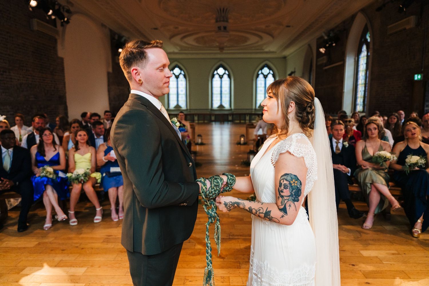 Wedding couple exchanges vows in front of gathered guests inside historic venue with wooden floors. PHOTOGRAPHER Dublin Ireland Wedding