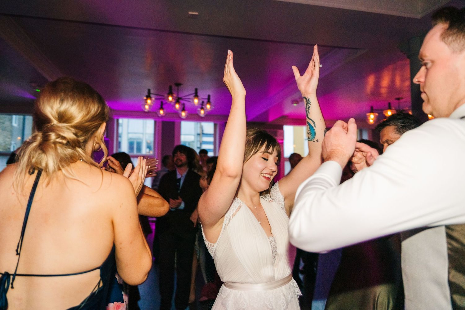 Wedding guests dancing and celebrating with raised hands under purple mood lighting. PHOTOGRAPHER Dublin Ireland Wedding